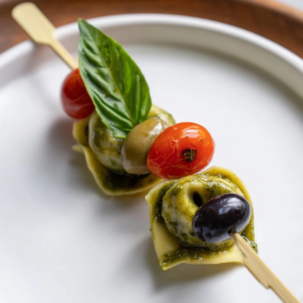Italian Appetizer Skewers feature pesto-coated tortellini, fresh basil, and olives ready for a summer party.