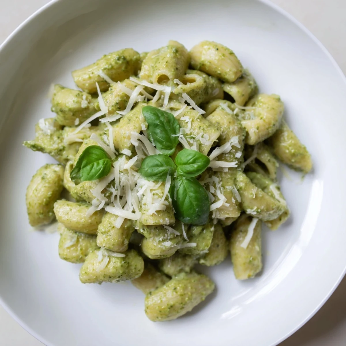 A close-up of Creamy Avocado Pesto Mac in a white bowl, showcasing the vibrant green sauce coating every piece of tender pasta, garnished with fresh basil.