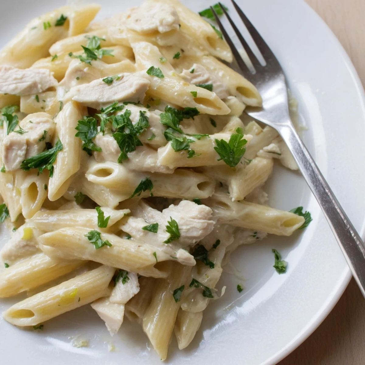 Garlicky penne pasta with tender roasted chicken slices, topped with fresh parsley on a cozy plate.