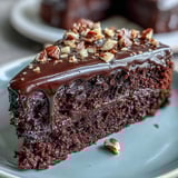 A plated slice of Chocolate Celebration Cake reveals tender crumb, dark chocolate ganache, and sparkling hazelnut praline shards. 