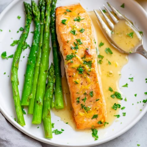 Skillet Lemon-Butter Salmon, glistening, is served atop vibrant green asparagus with lemon slices.