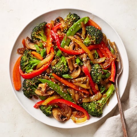 A close-up of vibrant ginger stir-fried vegetables glistening with sauce, served in a white bowl over steamed jasmine rice.