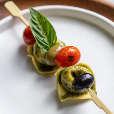 Italian Appetizer Skewers feature pesto-coated tortellini, fresh basil, and olives ready for a summer party.