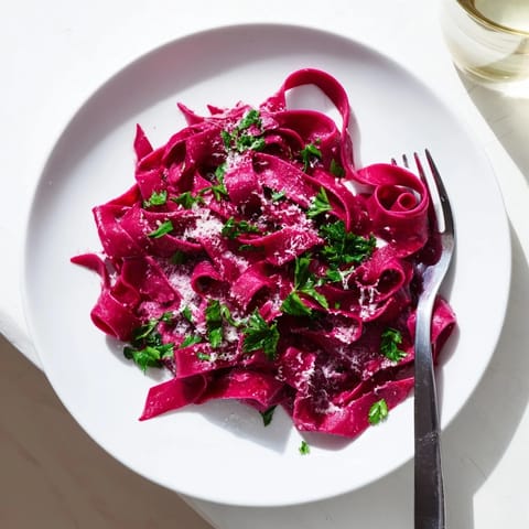 A rustic plate of Beet Noodle Pasta tossed with butter and fresh parsley sits beside a glass of white wine.  