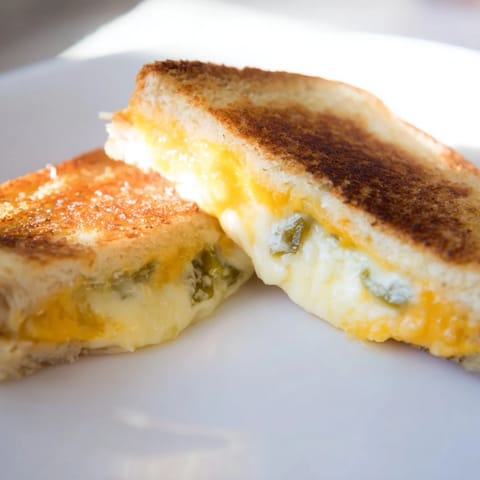 Close-up of a crispy Jalapeño Popper Grilled Cheese sandwich, showcasing the gooey, melted cheese filling oozing between golden bread.  