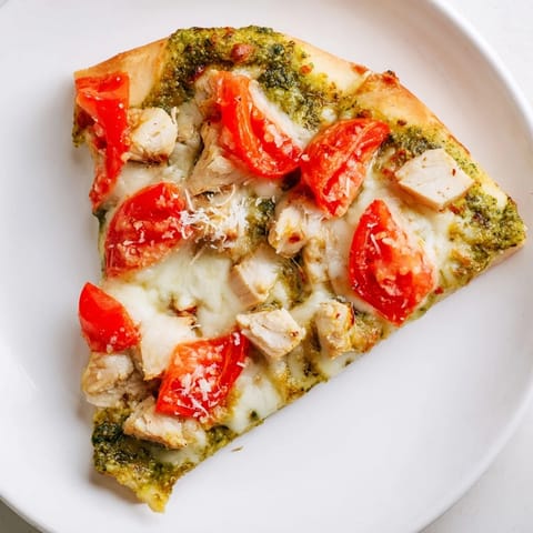 Homemade Chicken Pesto Pizza fresh from the oven, garnished with basil and ready to slice for a family dinner.  