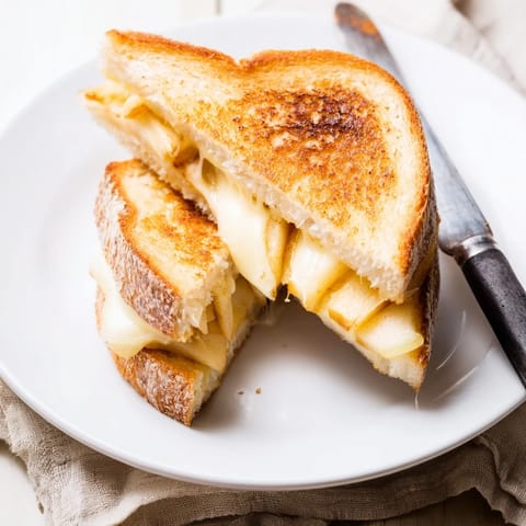 A warm, buttery Smoked Gouda & Apple Grilled Cheese sandwich is sliced to reveal gooey cheese and thinly sliced tart apples inside. 