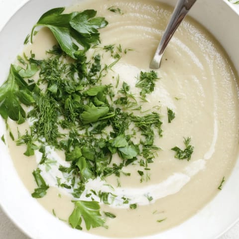 Warm parsnip and herb soup in a rustic bowl, topped with a swirl of cream and vibrant green herbs.