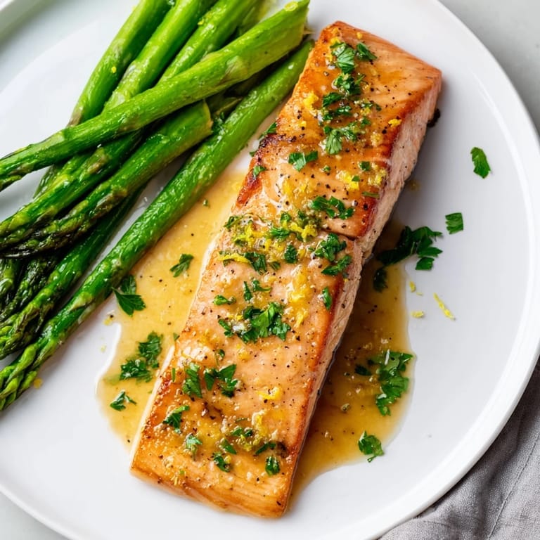 A close-up of tender Skillet Lemon-Butter Salmon, perfectly cooked alongside seasoned asparagus.