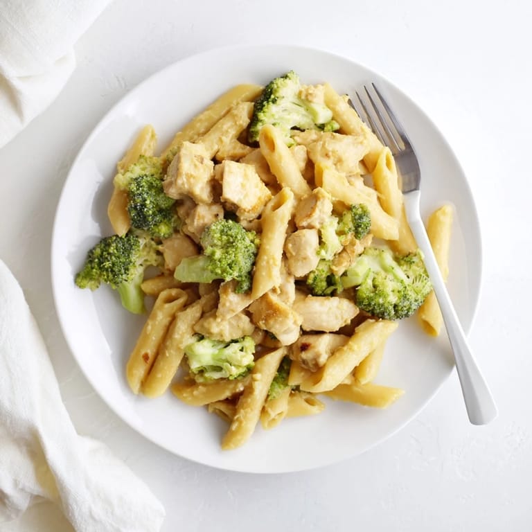 Savory Chicken Broccoli Cheddar Pasta served in a white bowl, steam rising from the cheesy penne, broccoli, and succulent chicken pieces, ready for a family dinner.